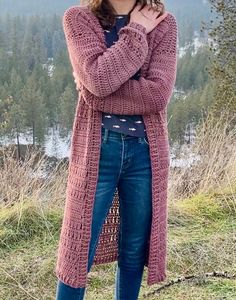 a woman standing on top of a grass covered hillside wearing a pink sweater and jeans