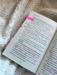 an open book sitting on top of a bed next to a white blanket with pink writing