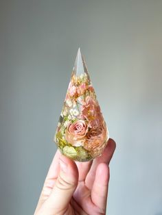 a hand holding a small glass vase with flowers on it in front of a gray background