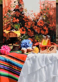 a painting of flowers and fruit on a table with a striped blanket in the foreground