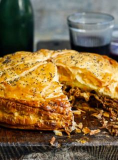 a meat and cheese pie is cut in half on a cutting board next to a bottle of wine