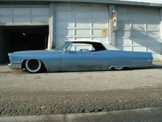 an old blue car parked in front of a garage