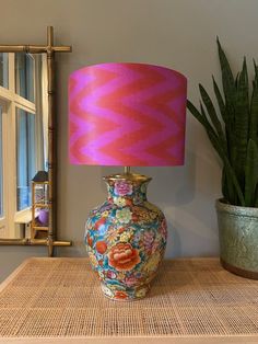 a pink lamp sitting on top of a wooden table next to a potted plant