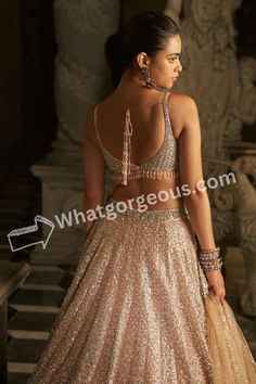 a woman in a gold and silver dress standing next to a pillar with her back turned