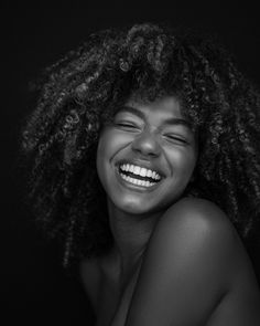 a black and white photo of a woman with curly hair smiling at the camera while she has her eyes closed