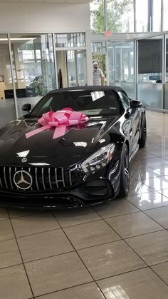 a black car with a pink bow on it's hood in a showroom