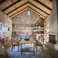 a dining room table and chairs in front of a stone wall with exposed beams on the ceiling