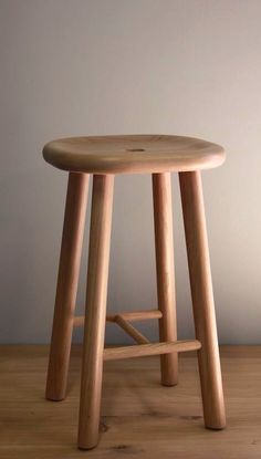 a wooden stool sitting on top of a hard wood floor next to a white wall