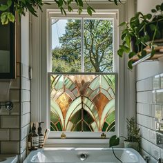 a bath tub sitting under a bathroom window next to a white sink and green plants