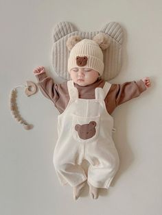 a baby laying on its back wearing a bear hat and overalls with ears attached