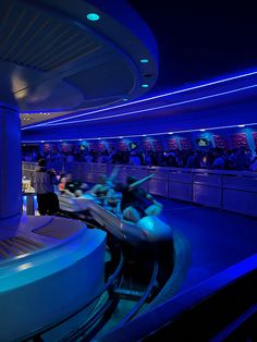 people are riding on roller coasters in an amusement park at night with blue lights