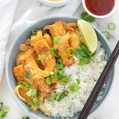 a blue bowl filled with rice and meat next to chopsticks on a white table