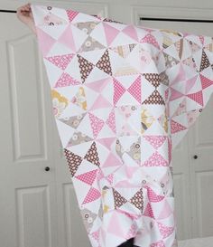 a woman is holding up a pink and white piece of fabric that has triangles on it