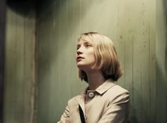 a woman standing in front of a green wall with her hands on her hips and looking up