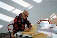 an older man sitting at a table working on some type of project with paper and scissors