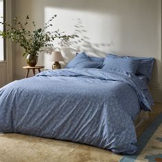 a bed with blue comforter and pillows in a room next to a plant on the floor