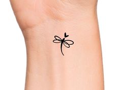 a small black tattoo on the wrist of a woman's left arm with a dragonfly