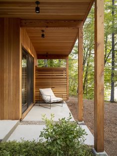 a covered porch with a chair on the side and trees in the backgroud