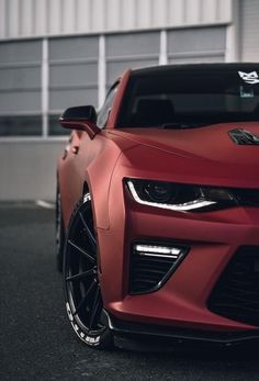 a red sports car parked in front of a white building with black rims on it