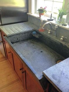 a kitchen sink sitting under a window next to a counter with a potted plant on it