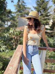 a woman wearing jeans and a straw hat leaning on a wooden rail in front of trees