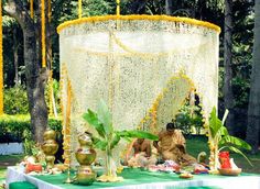 a man sitting in front of a white canopy covered with flowers and candles on top of a green table cloth