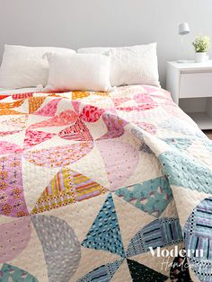 a bed with a colorful quilt on top of it next to a white night stand