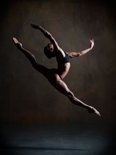 a male ballet dancer in the air with his arms extended and legs spread out,