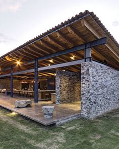 an outdoor dining area with stone walls and wooden roof, surrounded by green lawning