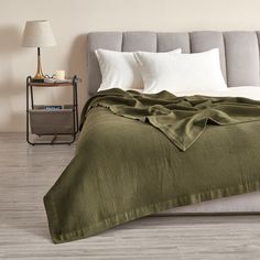 a bed with a green blanket on top of it next to a night stand and lamp