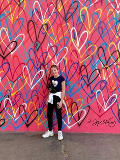 a girl standing in front of a wall with hearts painted on it