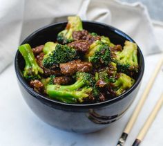 a bowl filled with beef and broccoli next to chopsticks