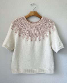 a white sweater hanging on a wall with a wooden hanger in front of it