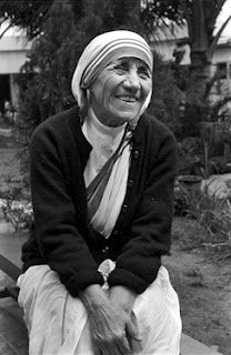 an old woman is sitting on a bench in front of some trees and bushes, smiling