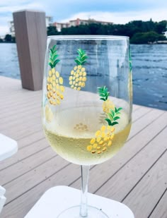 a wine glass sitting on top of a wooden table next to the water with yellow flowers painted on it