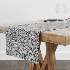 a wooden table topped with two wine glasses and a black and white patterned table cloth