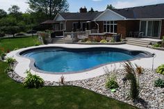 a backyard with a swimming pool surrounded by rocks and grass, next to a house