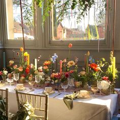 a table with flowers and candles is set up in front of a window for a party