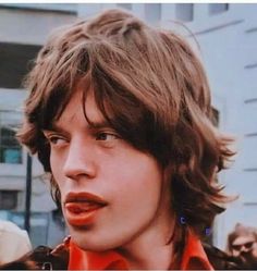 a close up of a person with long hair and an orange shirt in front of a building