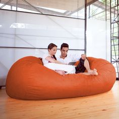 a man and woman sitting on an orange bean bag chair in the middle of a room