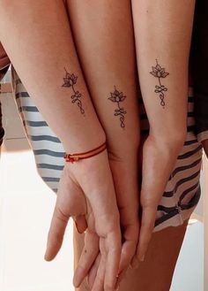 two women holding hands with tattoos on their arms and fingers, both showing the same tattoo