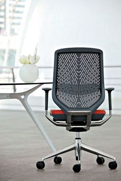 an office chair sitting in front of a table with a vase on top of it