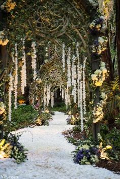 an outdoor garden with lots of flowers and greenery on the walkway, surrounded by trees