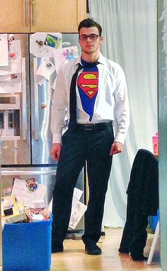 a young man dressed up as superman standing in front of a refrigerator with his hands on his hips