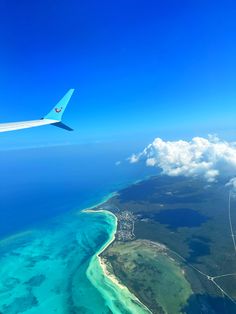 an airplane wing flying over the ocean and land area with blue water in the foreground