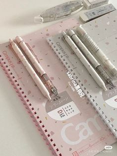 three pens sitting on top of a pink notebook next to a pen and pencil sharpener