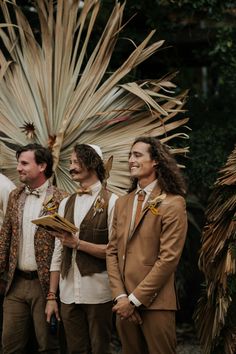 three men standing next to each other in front of palm trees and wearing brown suits