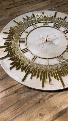 a clock that is on top of a wooden floor with roman numerals and gold trim