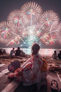 a woman sitting on the beach watching fireworks