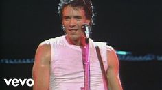 a man in white shirt and pink tie holding a microphone with his right hand on stage